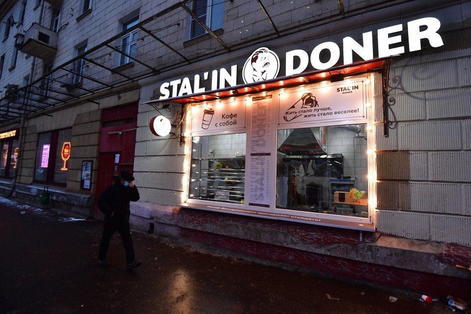 A man walks past a brightly-lit kebab stand called "Stalin Doner", with an image of Josef Stalin as the logo.