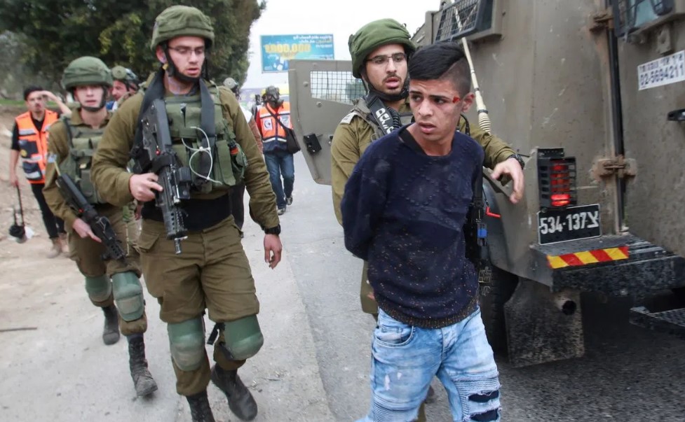 A young palestinian boy is escorted by Israeli soldiers while handcuffed
