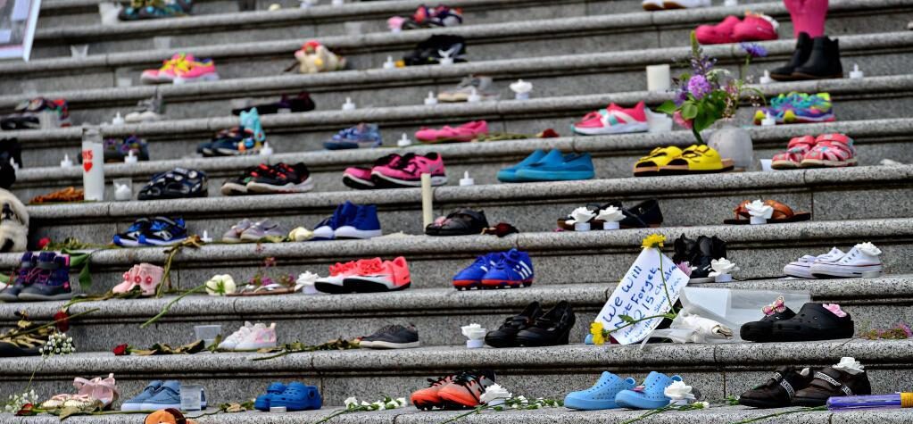 Children's shoes, notes, flowers, and candles are placed upon a concrete stairway in commemoration of 215 Indigenous children's bodies that were found at a former residential school.
